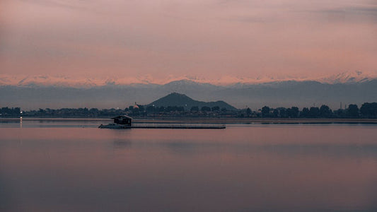 A serene lake view at sunset with distant mountains and a tranquil atmosphere.